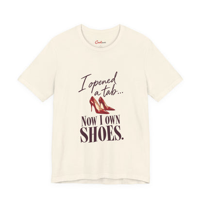 Natural Cooliooli T-shirt with red heels and “I opened a tab… Now I own shoes.” lettering, front flat lay