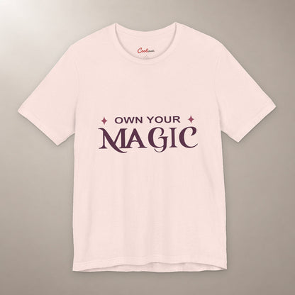 She's Got That Something. Bella+Canvas 3001 T-shirt in Soft Pink, front flat lay with Own Your Magic lettering and two rose-coloured stars on a plain warm neutral background.