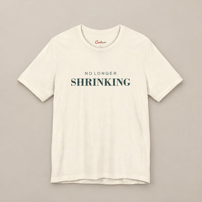Natural NO LONGER SHRINKING Bella+Canvas 3001 tee, complete square flat lay with deep green lettering on a plain warm neutral background.