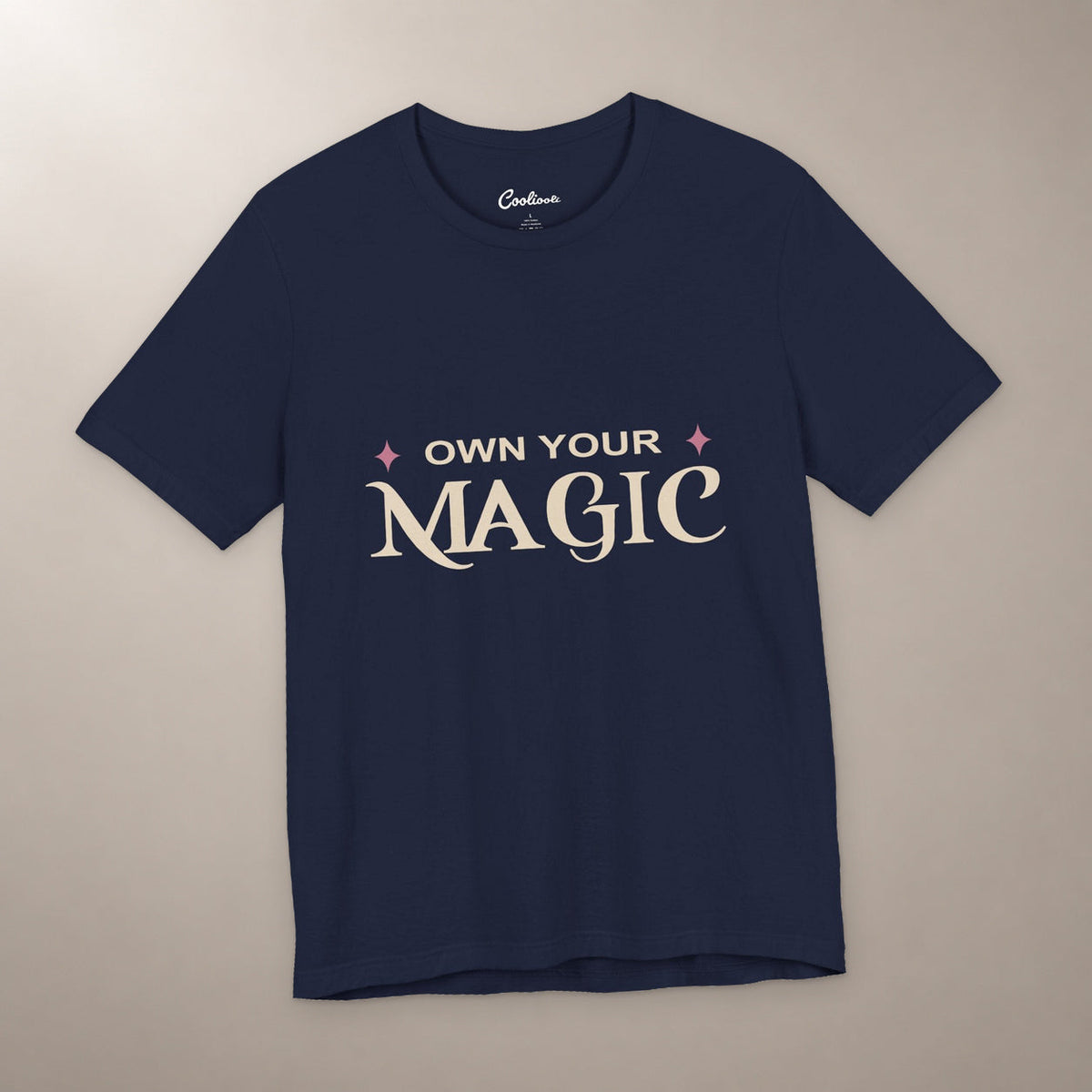 She's Got That Something. Bella+Canvas 3001 T-shirt in Navy, front flat lay with Own Your Magic lettering and two rose-coloured stars on a plain warm neutral background.