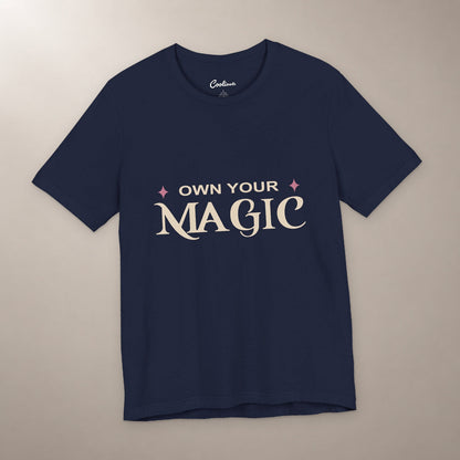 She's Got That Something. Bella+Canvas 3001 T-shirt in Navy, front flat lay with Own Your Magic lettering and two rose-coloured stars on a plain warm neutral background.