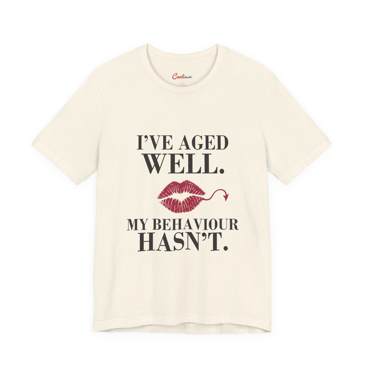 Natural Cooliooli Bella+Canvas 3001 T-shirt with “I’ve aged well. My behaviour hasn’t.” lettering and lipstick kiss with devil tail, front flat lay