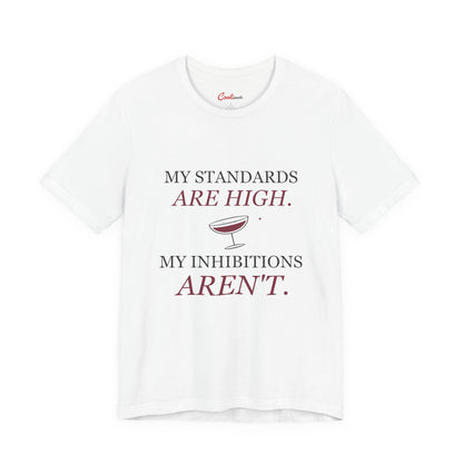 White Cooliooli Bella+Canvas 3001 tee with My standards are high. My inhibitions aren't. lettering and tipped cocktail coupe graphic, front flat lay.