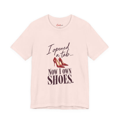 Soft Pink Cooliooli T-shirt with red heels and “I opened a tab… Now I own shoes.” lettering, front flat lay