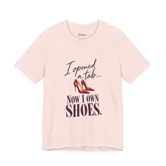 Soft Pink Cooliooli T-shirt with red heels and “I opened a tab… Now I own shoes.” lettering, front flat lay