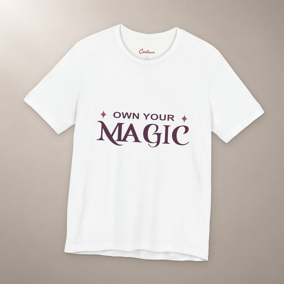 She's Got That Something. Bella+Canvas 3001 T-shirt in White, front flat lay with Own Your Magic lettering and two rose-coloured stars on a plain warm neutral background.