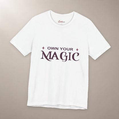 She's Got That Something. Bella+Canvas 3001 T-shirt in White, front flat lay with Own Your Magic lettering and two rose-coloured stars on a plain warm neutral background.