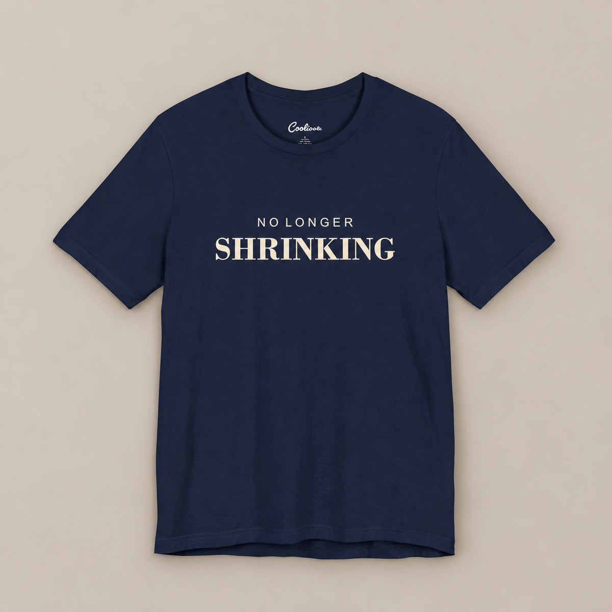 Navy NO LONGER SHRINKING Bella+Canvas 3001 tee, complete square flat lay with warm ivory lettering on a plain warm neutral background.