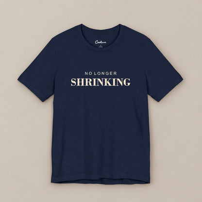 Navy NO LONGER SHRINKING Bella+Canvas 3001 tee, complete square flat lay with warm ivory lettering on a plain warm neutral background.