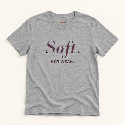 Soft. Not Weak. affirmation tee in Athletic Heather on a warm neutral studio background