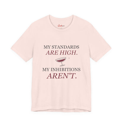 Soft Pink Cooliooli Bella+Canvas 3001 tee with My standards are high. My inhibitions aren't. lettering and tipped cocktail coupe graphic, front flat lay.