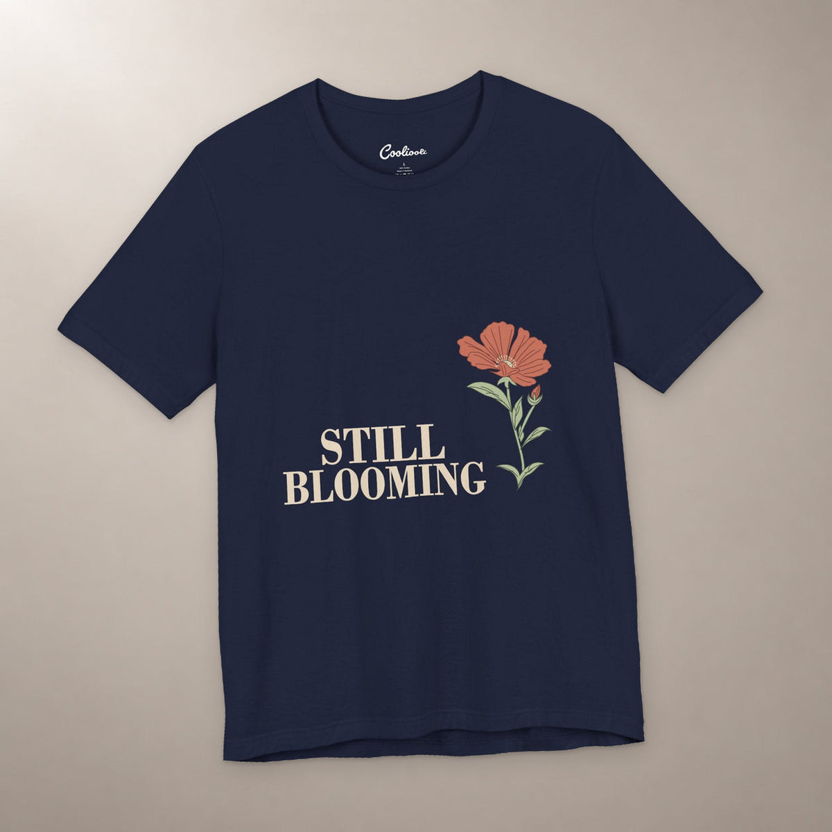 Still Coming Into Her Own. Bella+Canvas 3001 T-shirt in Navy, front flat lay with Still Blooming lettering and a brick-red poppy on a plain warm neutral background.