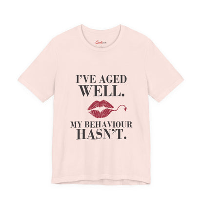 Soft Pink Cooliooli Bella+Canvas 3001 T-shirt with “I’ve aged well. My behaviour hasn’t.” lettering and lipstick kiss with devil tail, front flat lay