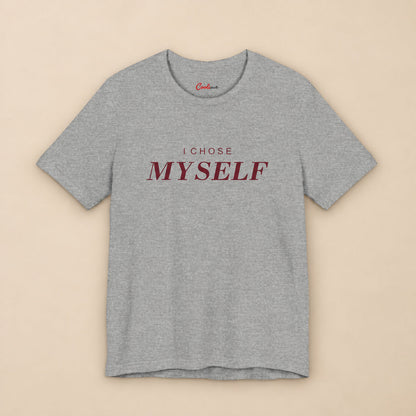Her First Choice. Athletic Heather Bella+Canvas 3001 T-shirt with burgundy I CHOSE MYSELF lettering and Cooliooli neck print, complete square flat lay on a warm neutral background.