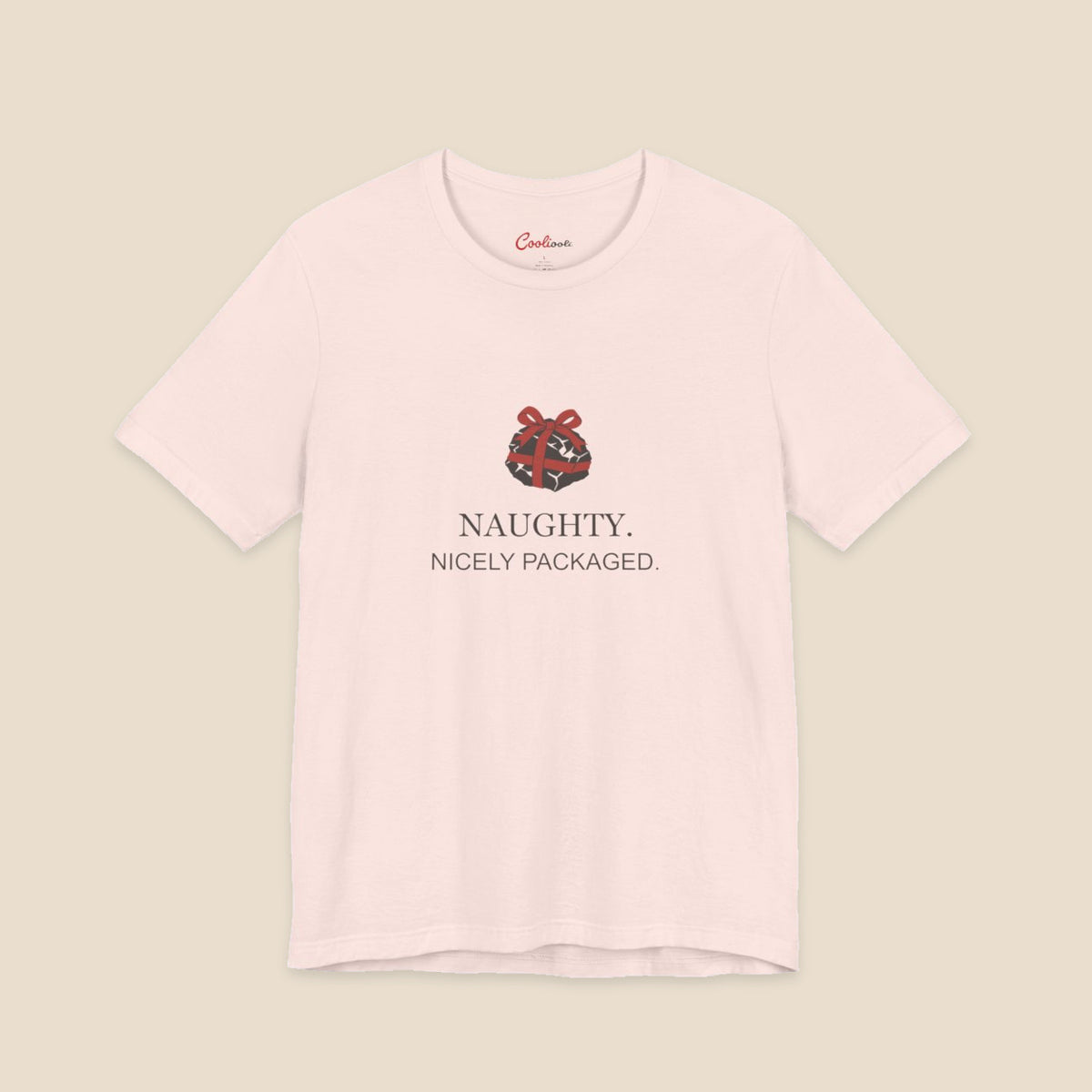 Soft Pink Bella+Canvas 3001 Christmas T-shirt with an original coal and red bow illustration above Naughty. Nicely Packaged. lettering.