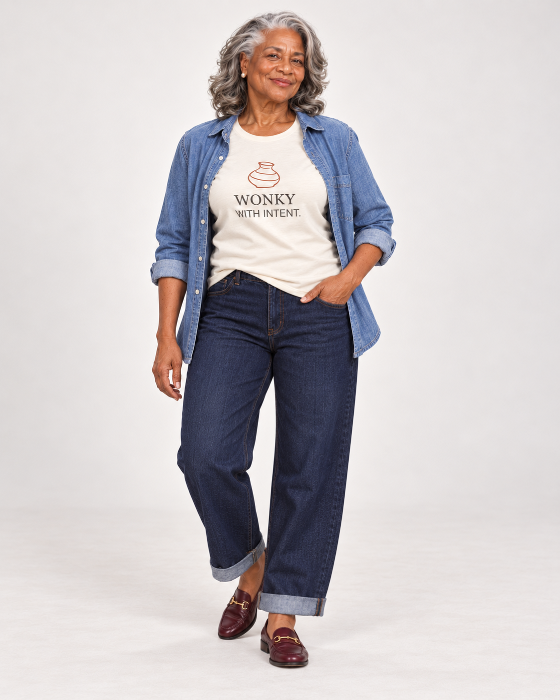 Vivienne wearing the Natural Wonky With Intent pottery T-shirt with an open blue overshirt, cuffed dark barrel jeans and burgundy loafers.