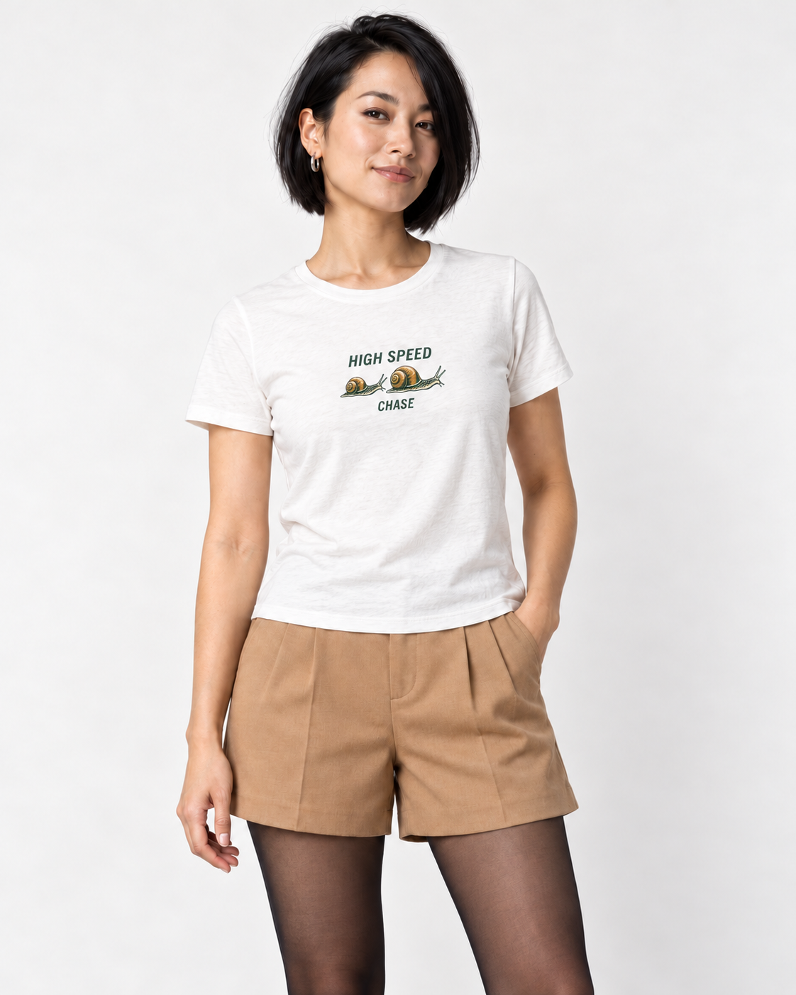 Mina wearing the White HIGH SPEED CHASE two-snail Bella+Canvas 6400 women’s relaxed-fit tee with camel tailored shorts and sheer black tights in a pale studio.