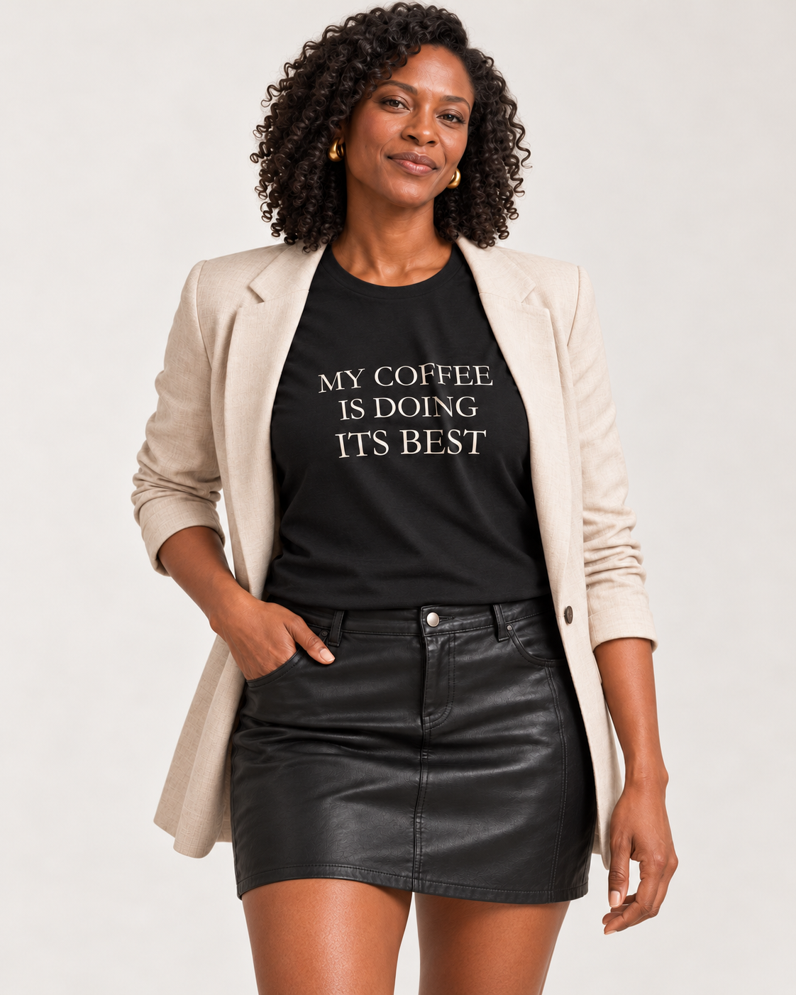 Amara wearing the Black My Coffee Is Doing Its Best Bella+Canvas3001 tee with an open beige blazer and black mini skirt.