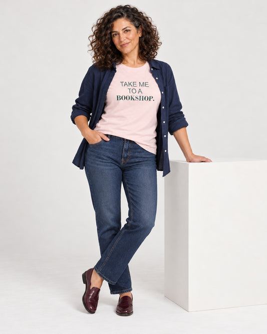 Leila wearing the Soft Pink Bella+Canvas3001 T-shirt with dark straight-leg jeans, burgundy loafers, relaxed open navy overshirt kept well clear of the print. Exact print: TAKE ME TO A BOOKSHOP.
