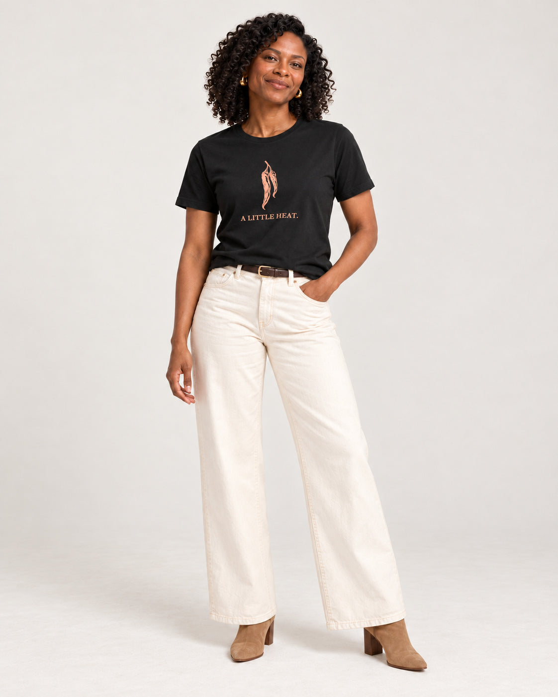 Amara wearing the Black Bella+Canvas3001 T-shirt with ecru wide-leg jeans with tan heeled ankle boots and a slim dark belt. Exact print: A LITTLE HEAT.