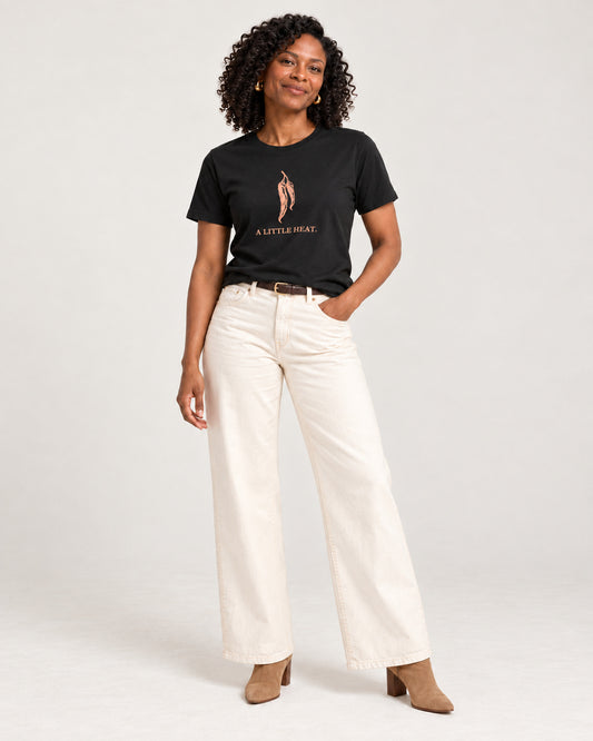 Amara wearing the Black Bella+Canvas3001 T-shirt with ecru wide-leg jeans with tan heeled ankle boots and a slim dark belt. Exact print: A LITTLE HEAT.