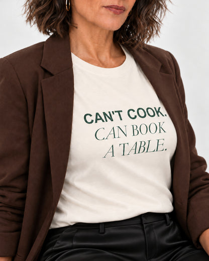Close-up of the Natural Can't Cook, Can Book a Table tee, showing matte forest-green lettering following the jersey.