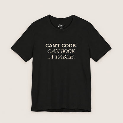 Can't Cook, Can Book a Table Bella+Canvas 3001 T-shirt in Black, front flat lay.