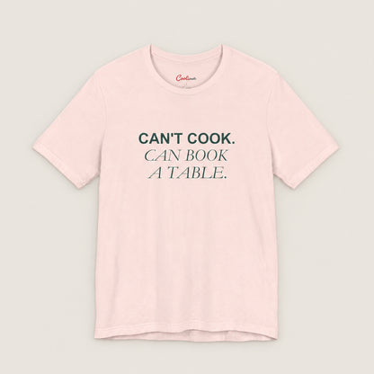 Can't Cook, Can Book a Table Bella+Canvas 3001 T-shirt in Soft Pink, front flat lay.