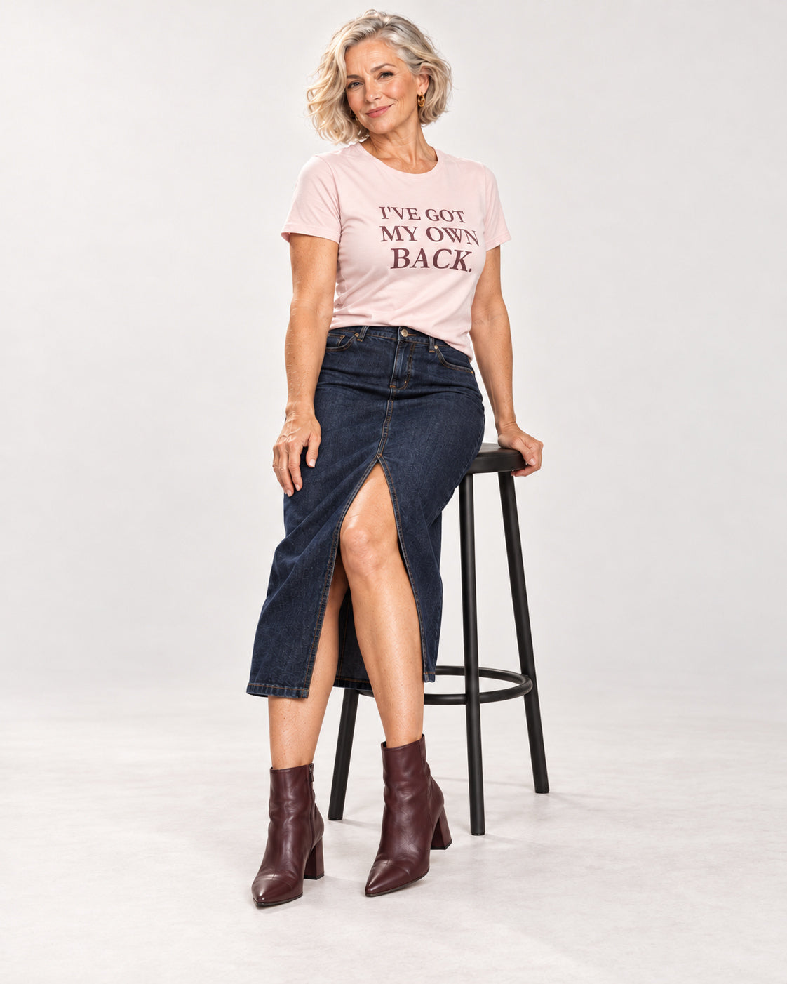 Claudia wearing the Soft Pink I'VE GOT MY OWN BACK. Bella+Canvas 3001 tee, with a denim midi skirt and heeled boots.