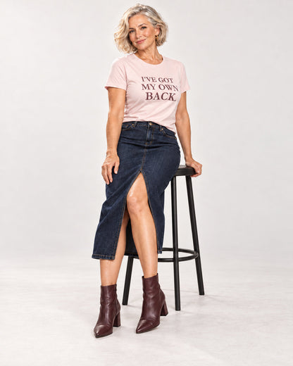 Claudia wearing the Soft Pink I'VE GOT MY OWN BACK. Bella+Canvas 3001 tee, with a denim midi skirt and heeled boots.
