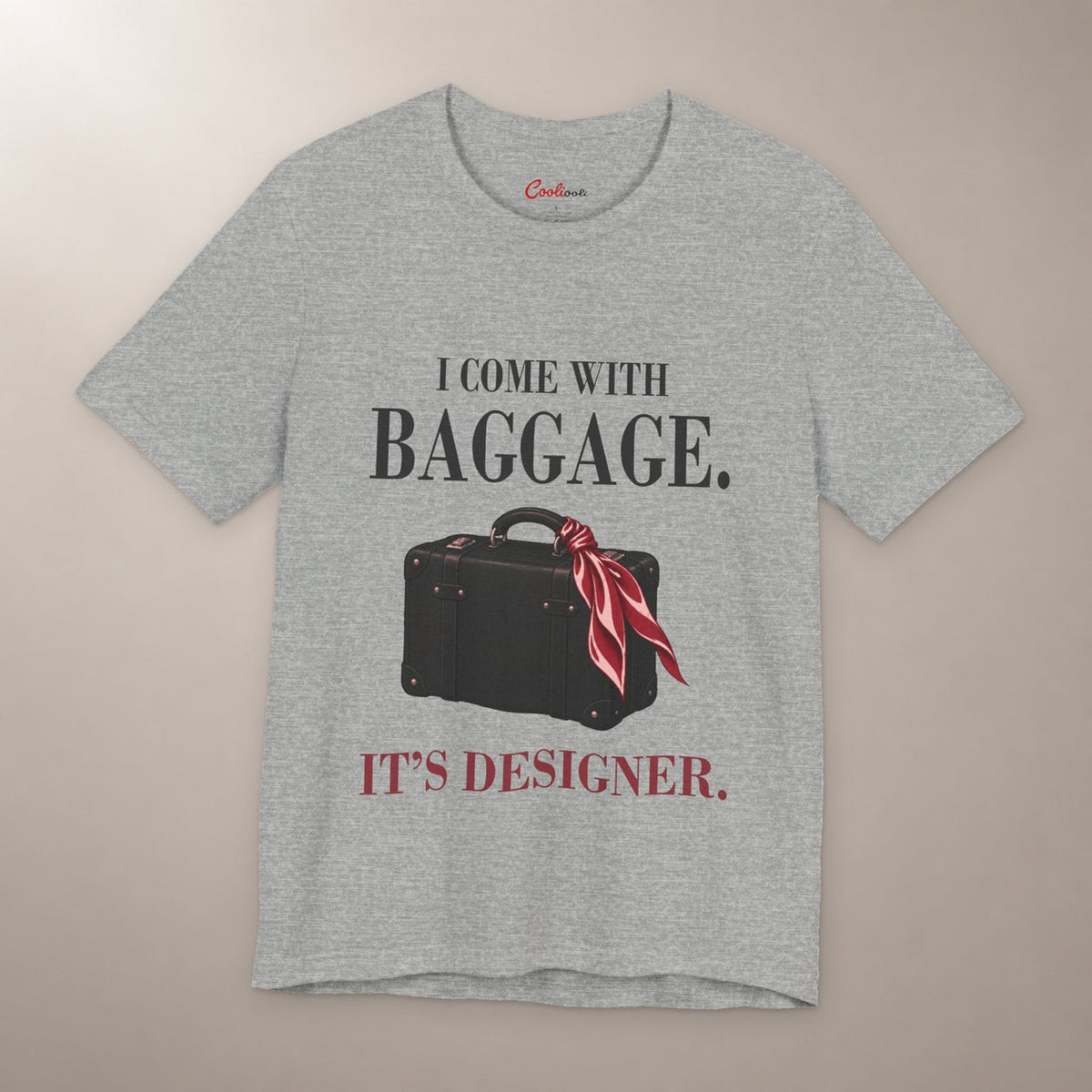 Excess Baggage. Excellent Taste. Bella+Canvas 3001 T-shirt in Athletic Heather, front flat lay with I come with baggage. It’s designer. lettering and a vintage suitcase with a burgundy scarf on a plain warm neutral background.