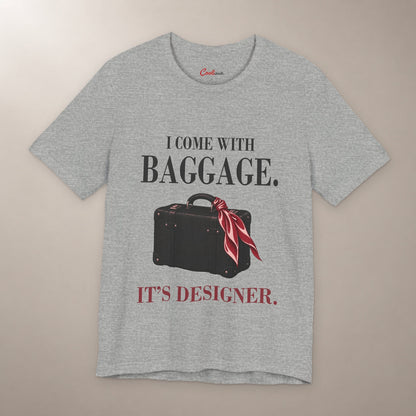 Excess Baggage. Excellent Taste. Bella+Canvas 3001 T-shirt in Athletic Heather, front flat lay with I come with baggage. It’s designer. lettering and a vintage suitcase with a burgundy scarf on a plain warm neutral background.