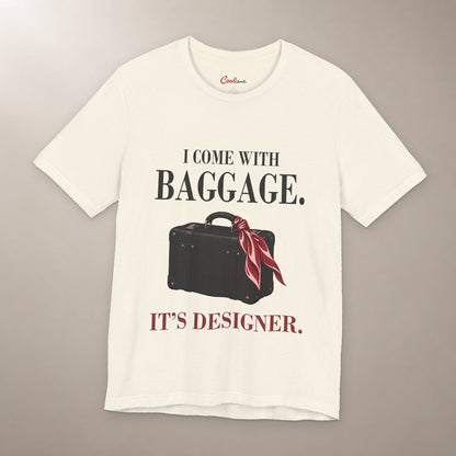 Excess Baggage. Excellent Taste. Bella+Canvas 3001 T-shirt in Natural, front flat lay with I come with baggage. It’s designer. lettering and a vintage suitcase with a burgundy scarf on a plain warm neutral background.