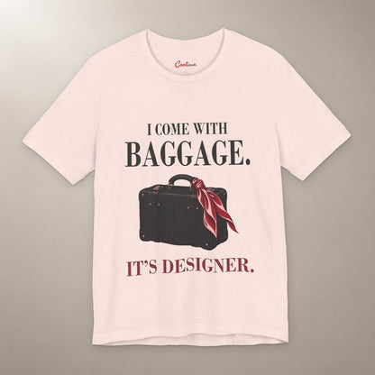 Excess Baggage. Excellent Taste. Bella+Canvas 3001 T-shirt in Soft Pink, front flat lay with I come with baggage. It’s designer. lettering and a vintage suitcase with a burgundy scarf on a plain warm neutral background.