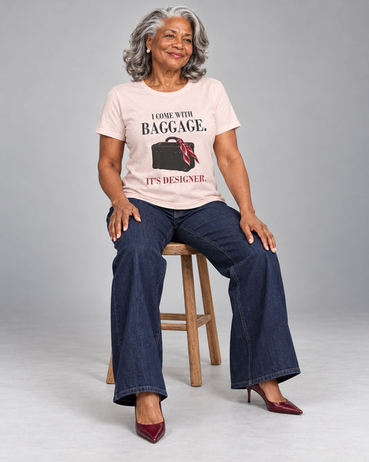 Vivienne wearing the Soft Pink Designer Baggage Bella+Canvas 3001 tee with wide-leg jeans and burgundy heels, seated naturally during a professional studio photoshoot.