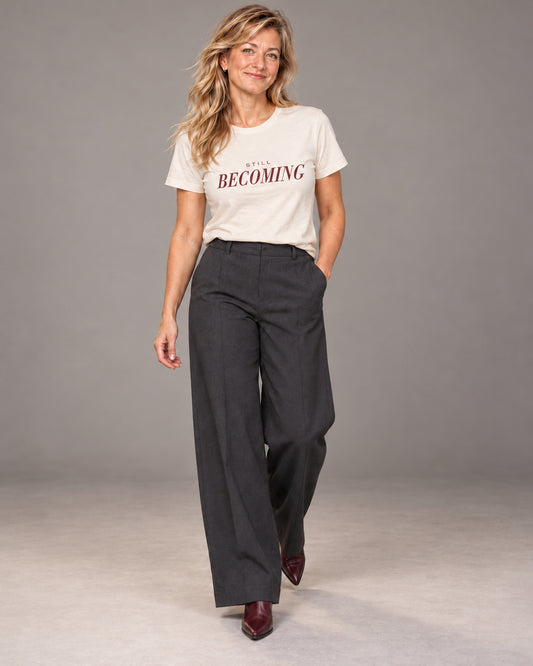 Elena wearing the Natural Still Becoming Bella+Canvas 3001 T-shirt with charcoal wide-leg trousers and burgundy heeled ankle boots, full-length studio portrait.