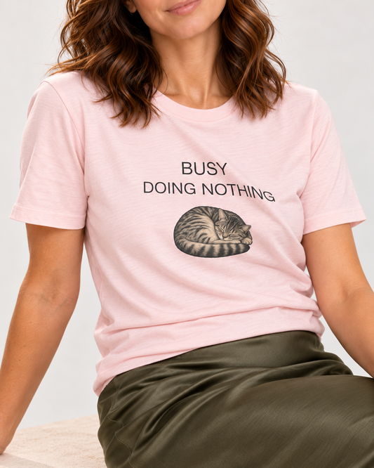 Close-up of the Soft Pink Busy Doing Nothing tee with curled tabby graphic and matte lettering following a cotton fold.