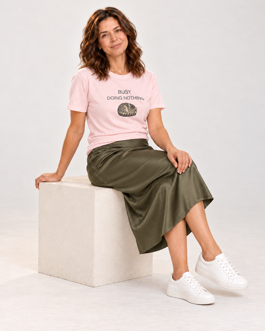Sophie seated in the Soft Pink Busy Doing Nothing sleeping-cat T-shirt, olive satin midi skirt and white trainers.