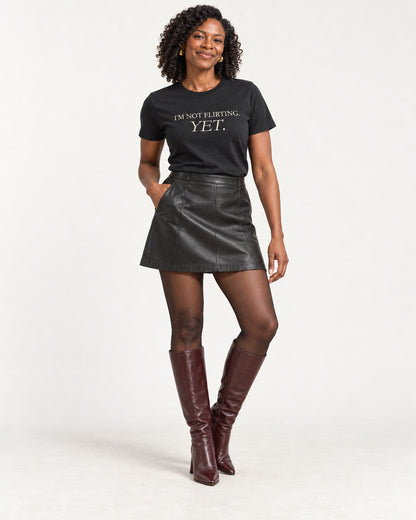 Amara wearing the black I'm Not Flirting Yet T-shirt with a leather-look mini and burgundy heeled boots