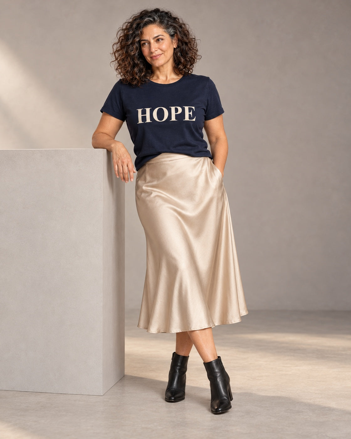 Leila wearing the Navy HOPE Bella+Canvas 3001 tee with a satin midi skirt and black ankle boots, full-length studio portrait.