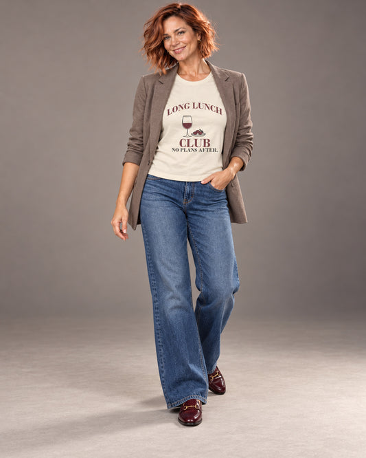 Sienna wearing the Natural Long Lunch Club Bella+Canvas 3001 tee with wide-leg jeans and a relaxed blazer in a full-length professional studio photograph.