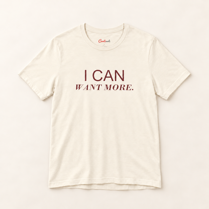 I CAN WANT MORE. Bella+Canvas 3001 tee in Natural, overhead view on a plain warm neutral studio background