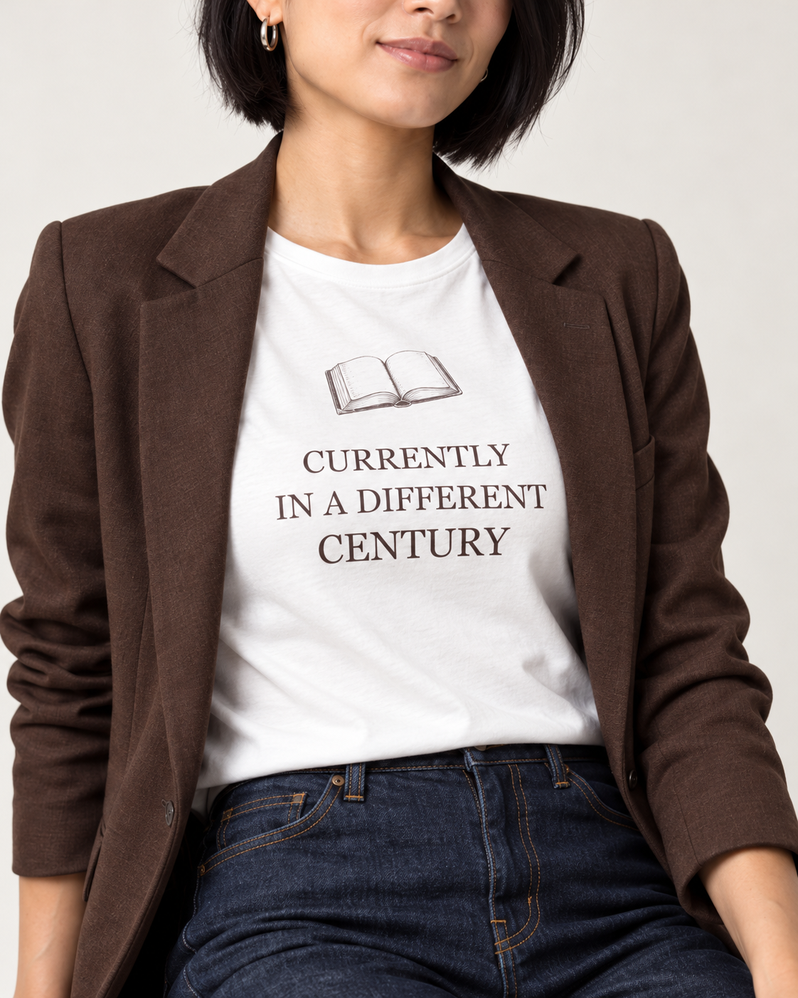 Close detail of the White Bella+Canvas 3001 T-shirt with an original open book and Currently in a Different Century lettering.