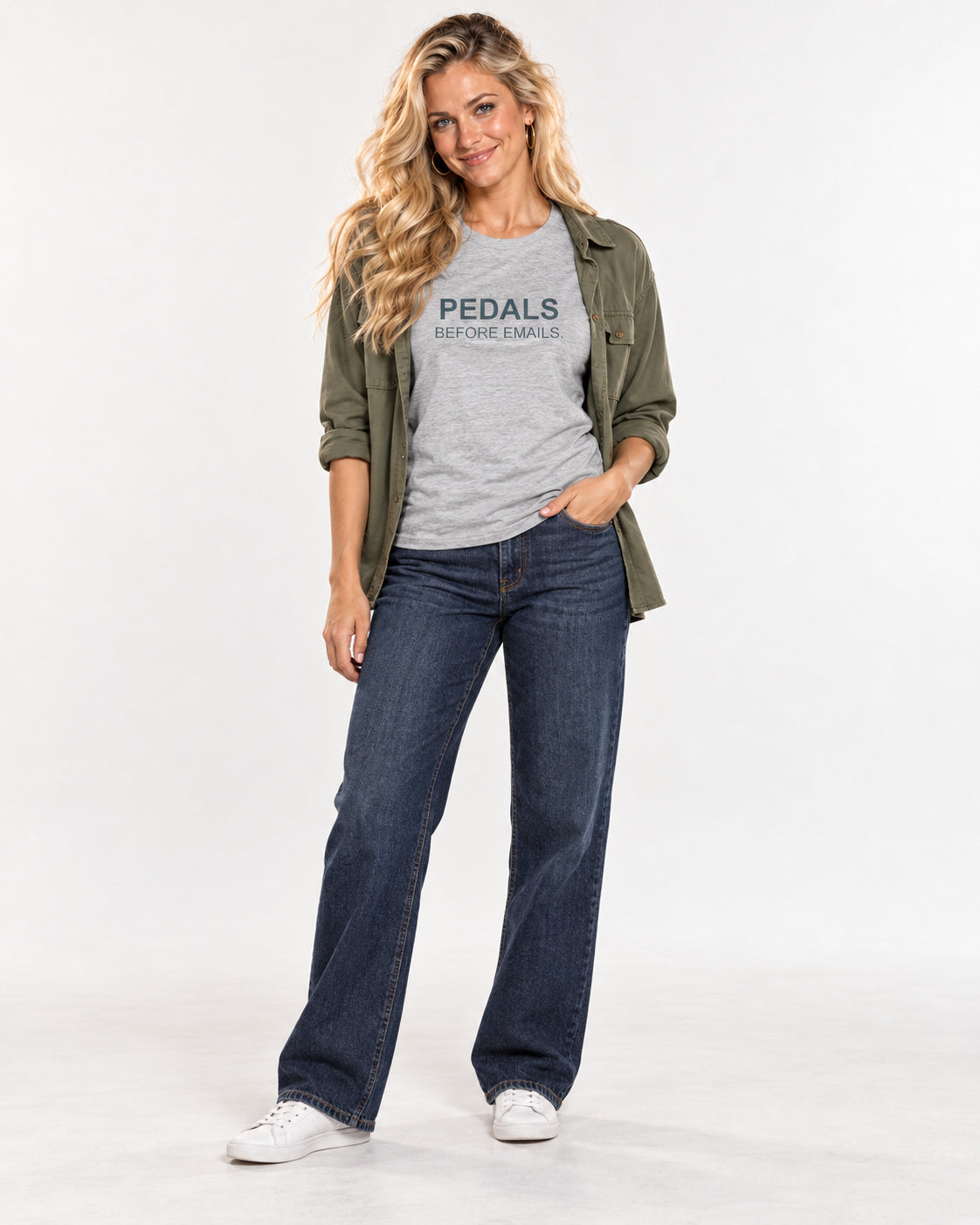 Chloe wearing the Athletic Heather Pedals Before Emails. Bella+Canvas3001 T-shirt with an open olive overshirt, dark blue jeans and white trainers.