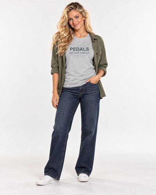 Chloe wearing the Athletic Heather Pedals Before Emails. Bella+Canvas3001 T-shirt with an open olive overshirt, dark blue jeans and white trainers.