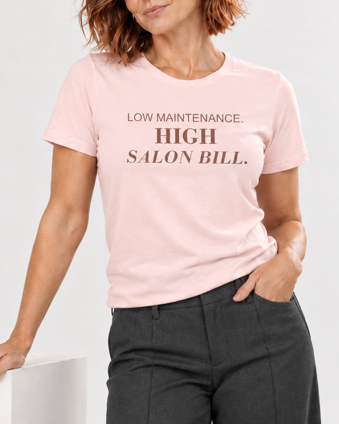 Sienna wearing the Soft Pink LOW MAINTENANCE. HIGH SALON BILL. Bella+Canvas 3001 tee — collar-to-hip studio detail showing the print following fabric folds