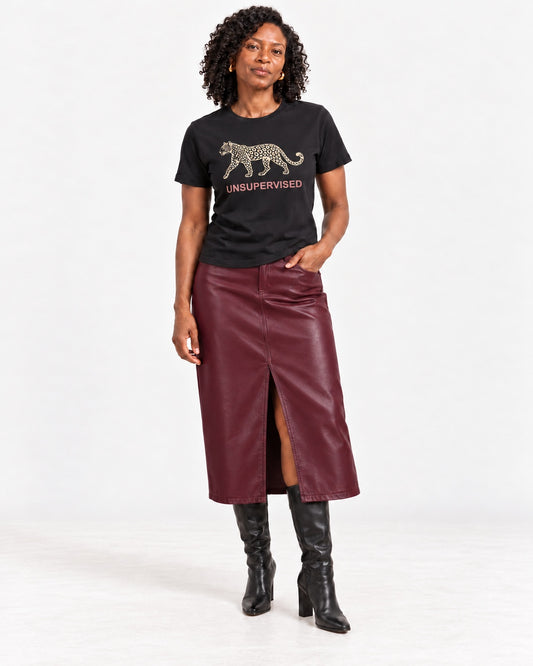 Amara wearing the Black UNSUPERVISED leopard Bella+Canvas 3001 tee with a leather-look midi skirt and tall heeled boots in a natural studio