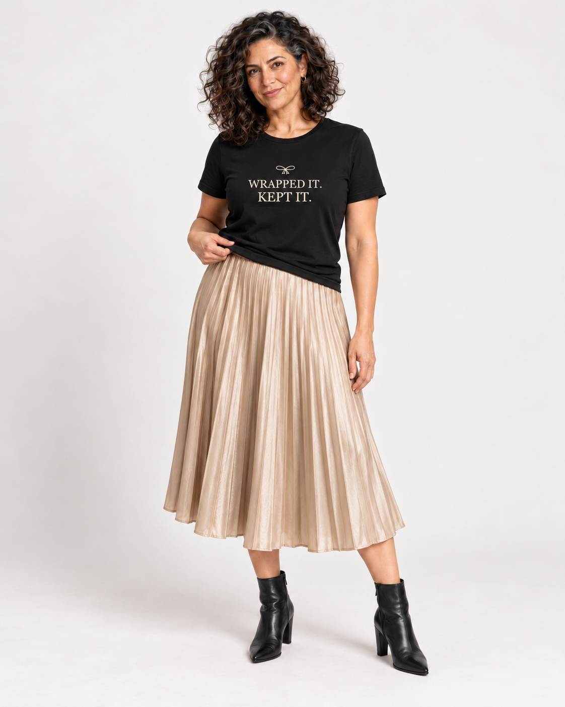 Leila wearing the Black Wrapped It. Kept It. Christmas bow T-shirt with a champagne pleated midi skirt and black ankle boots.