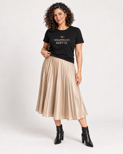 Leila wearing the Black Wrapped It. Kept It. Christmas bow T-shirt with a champagne pleated midi skirt and black ankle boots.