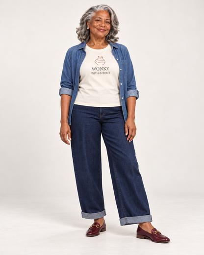 Vivienne wearing the Natural Wonky With Intent Bella+Canvas 6400 women’s relaxed-fit tee with an open blue overshirt, dark cuffed jeans and burgundy loafers.